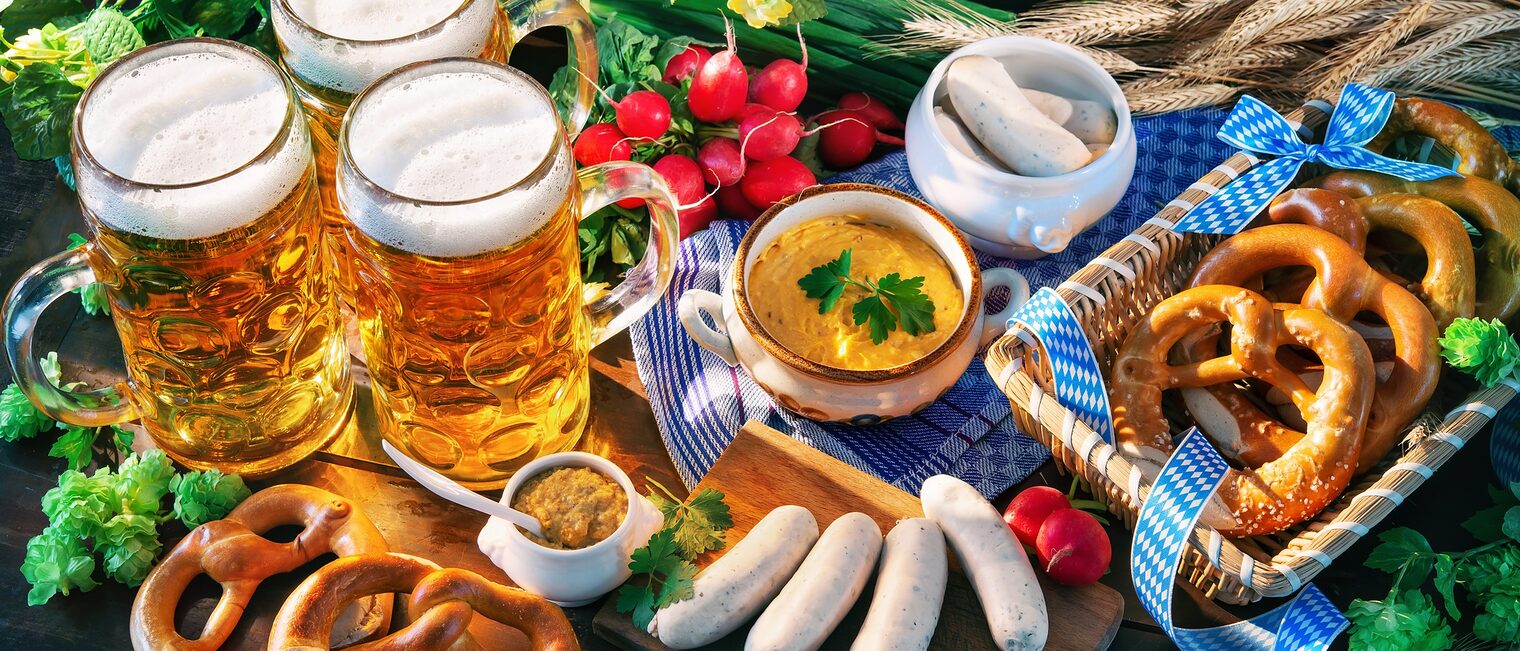 Bavarian sausages with pretzels, sweet mustard and beer mugs on rustic wooden table. Oktoberfest menu